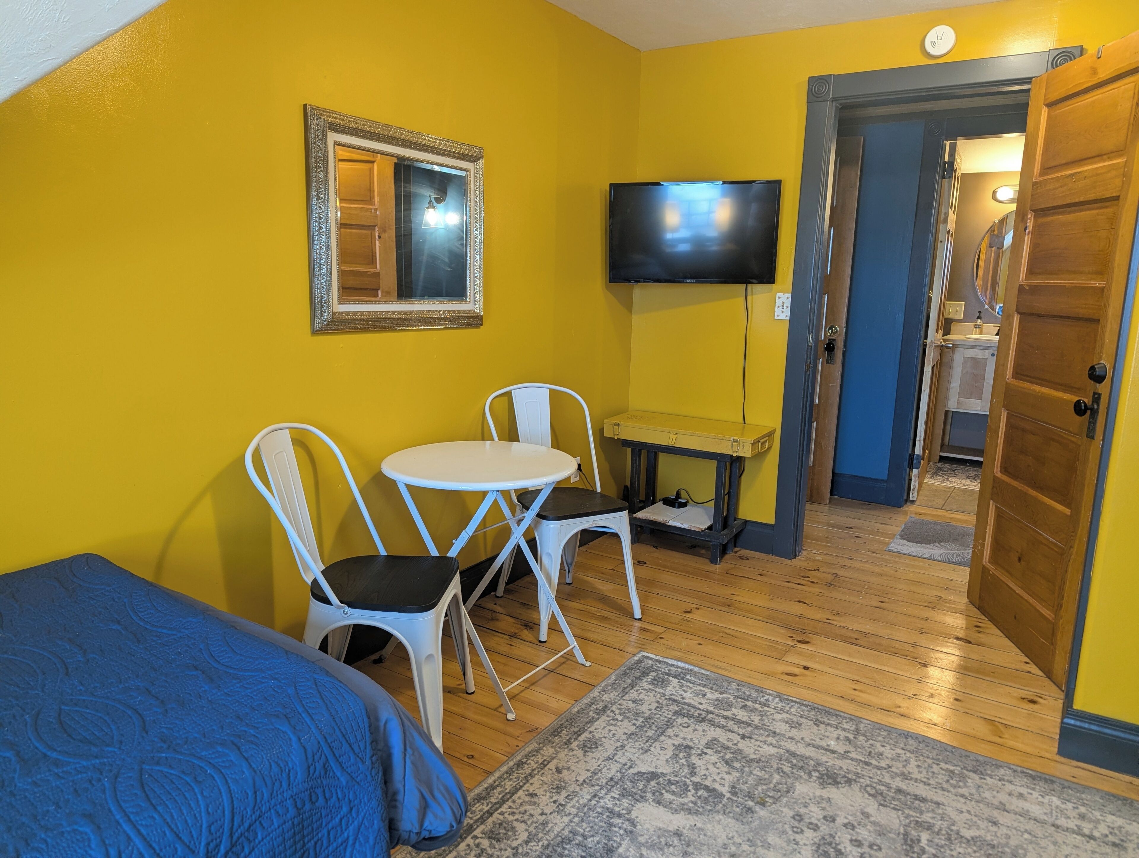 A room with a bed, a small table with chairs, a television, and a door leading to a bathroom.