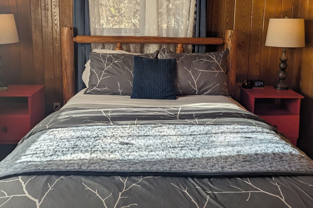 A wooden-paneled bedroom with a bed, two bedside tables, and a window with curtains.