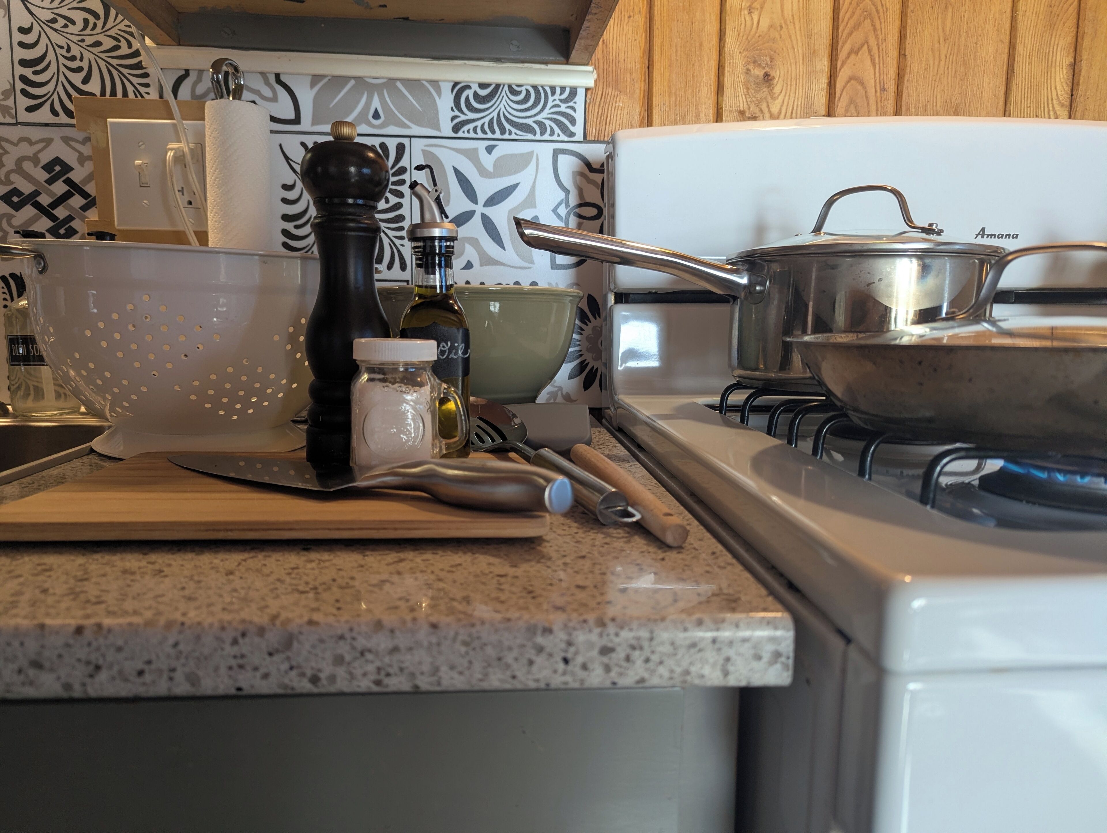 Una encimera de cocina con una hornilla, una olla, un molinillo de pimienta, una botella y un colador.