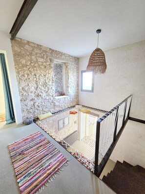 A room with a stone wall, a window, a hanging light fixture, a colorful rug, and a white crib. - Unique House in the Luberon with an Above-Ground Pool   (Robion)