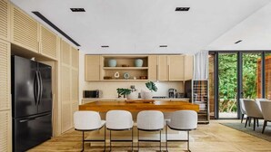 A modern kitchen with a central island, bar stools, and a black refrigerator. - Luxury 5Br Villa with Private Pool (Playa del Carmen)