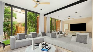 A modern living room with a grey sectional sofa, a round coffee table, and a flat-screen TV mounted on the wall. - Luxury 5Br Villa with Private Pool (Playa del Carmen)
