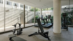 Een sportschool met trainingsapparatuur, waaronder loopbanden, een bankdrukrek en een squatsrek.