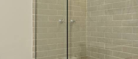 A glass-enclosed shower with a white tiled wall and a white toilet visible to the left.