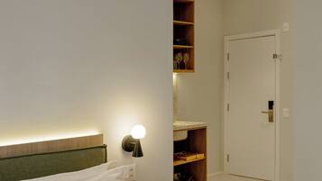 Habitación de hotel con cama, mesita de noche, lámpara de pared y una puerta que da a otra habitación.