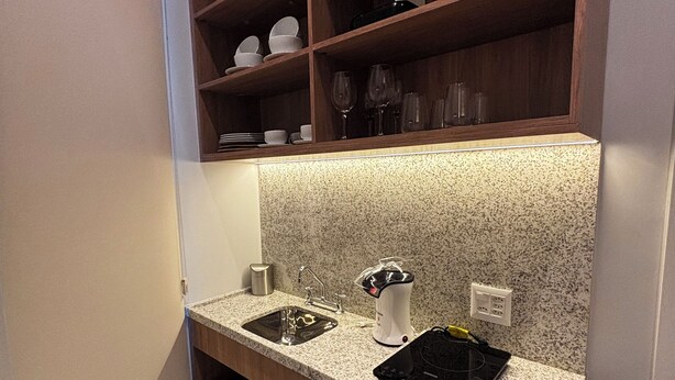 A compact kitchen with a granite countertop, two sinks, a built-in oven, and wooden shelves above. - Aloe Casa Jardins (São Paulo)