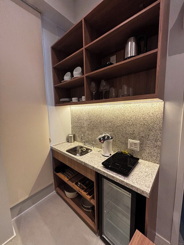 A compact kitchen with a granite countertop, two sinks, a built-in oven, and wooden shelves above. - Aloe Casa Jardins (São Paulo)