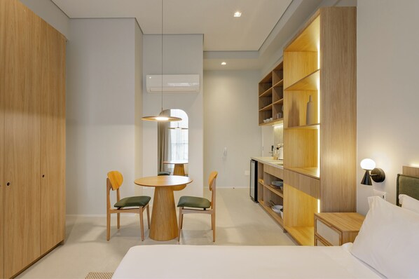 A modern hotel room with a bed, a dining table with chairs, a wardrobe, and a built-in bookshelf. - Aloe Casa Jardins (São Paulo)