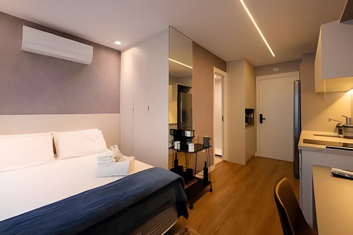 A hotel room with a bed, a desk, and a chair. There is a wardrobe and a mirror.