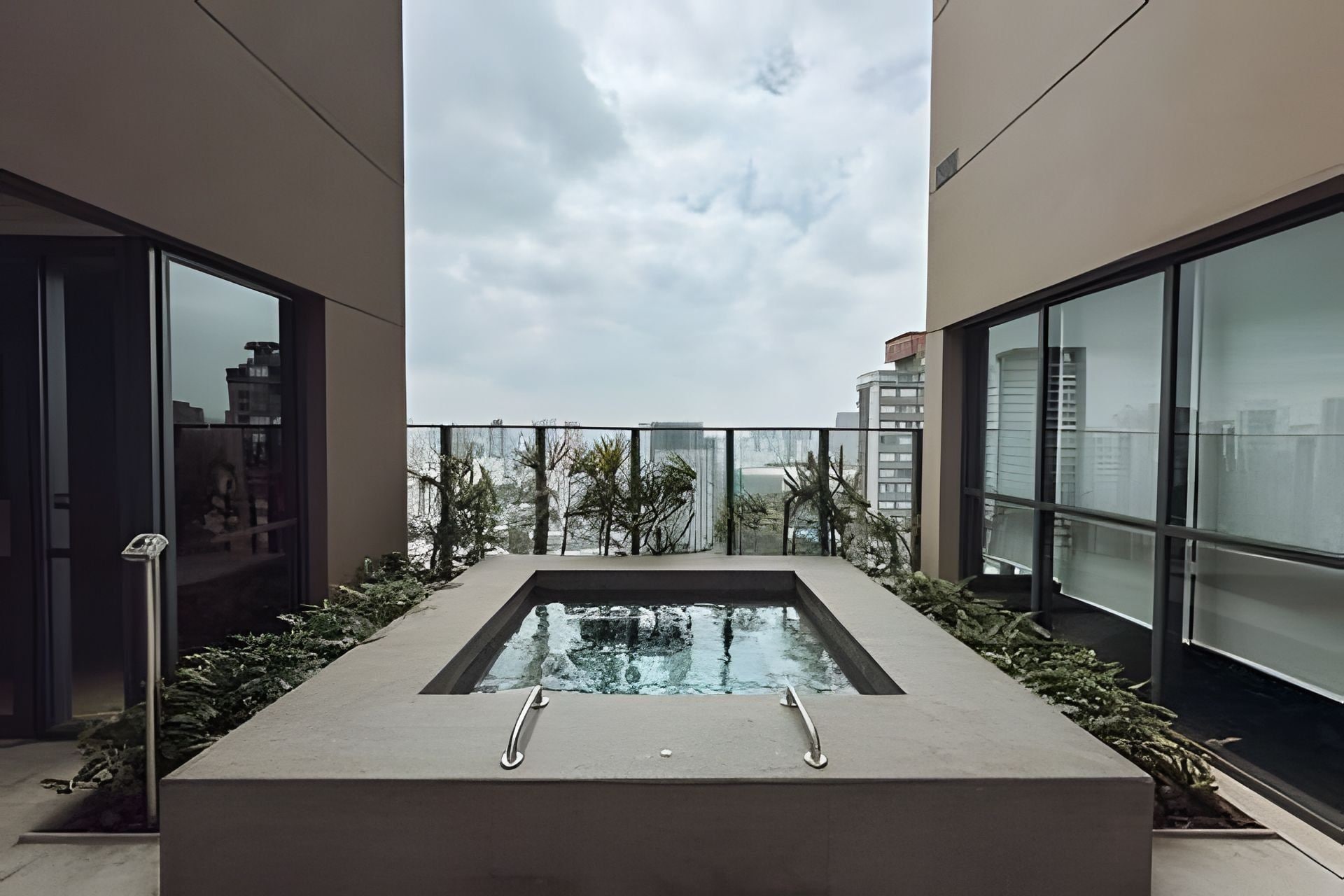Une piscine sur le toit, entourée d’une barrière en verre, de verdure et d’une architecture moderne.