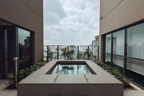 A rooftop pool with a glass barrier, surrounded by greenery and modern architecture. - SOMA PERDIZES 908 (São Paulo)
