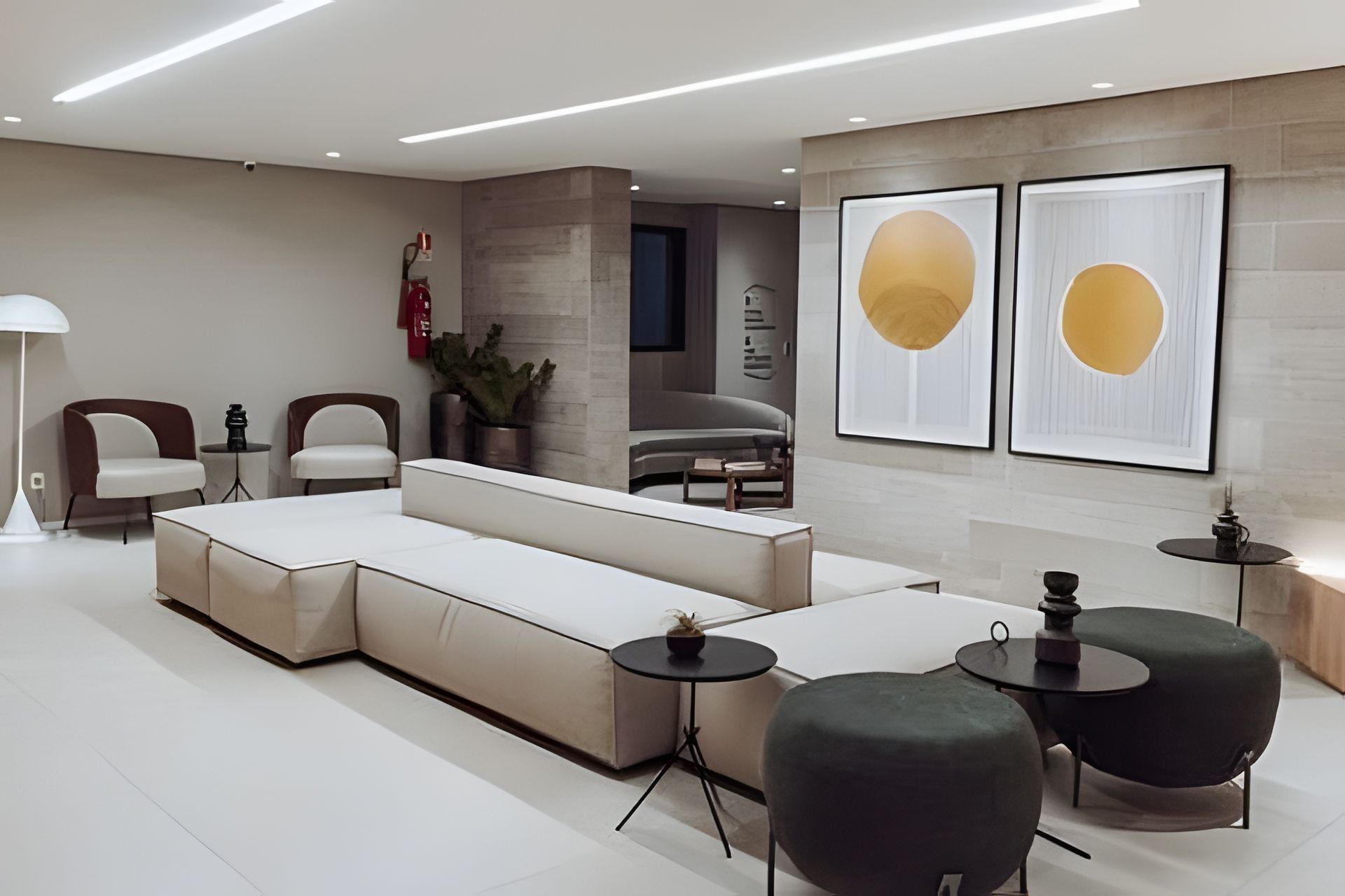 Un salon moderne comprenant un canapé d’angle, deux fauteuils, une table basse et une table d’appoint. Deux tableaux abstraits encadrés ornent le mur.