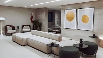 Un salon moderne comprenant un canapé d’angle, deux fauteuils, une table basse et une table d’appoint. Deux tableaux abstraits encadrés ornent le mur.