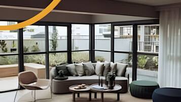 Una sala de estar moderna con sofá, mesa de centro y zona de estar, ventanas amplias y vistas al exterior.