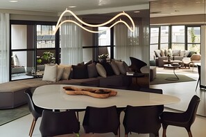 A modern living room with a sectional sofa, a dining table with chairs, and a large window providing natural light. - SOMA PERDIZES 908 (São Paulo)