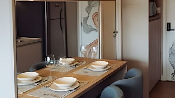 A dining area with a wooden table set for four, blue chairs, and a decorative wall. - SOMA PERDIZES 908 (São Paulo)
