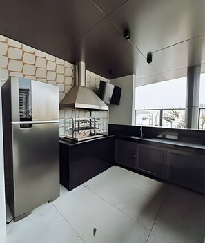 A modern kitchen with a built-in oven, a range hood, and a window overlooking a cityscape. - SOMA PERDIZES 908 (São Paulo)