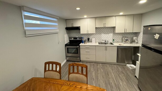 A modern kitchen with light-colored cabinets, a stainless steel refrigerator, and a dining area with a wooden table and chairs. - Cozy Ground Floor Flat (Kitchener)