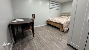 A bedroom with a bed, a desk with a chair, a lamp, and a window with blinds. - Cozy Ground Floor Flat (Kitchener)