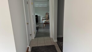 A hallway with a dark rug, a chair, and a television in the background. - Cozy Ground Floor Flat (Kitchener)
