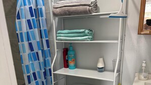 A bathroom with a toilet, a shower curtain, a shelf with towels, and toiletries. - Cozy Ground Floor Flat (Kitchener)
