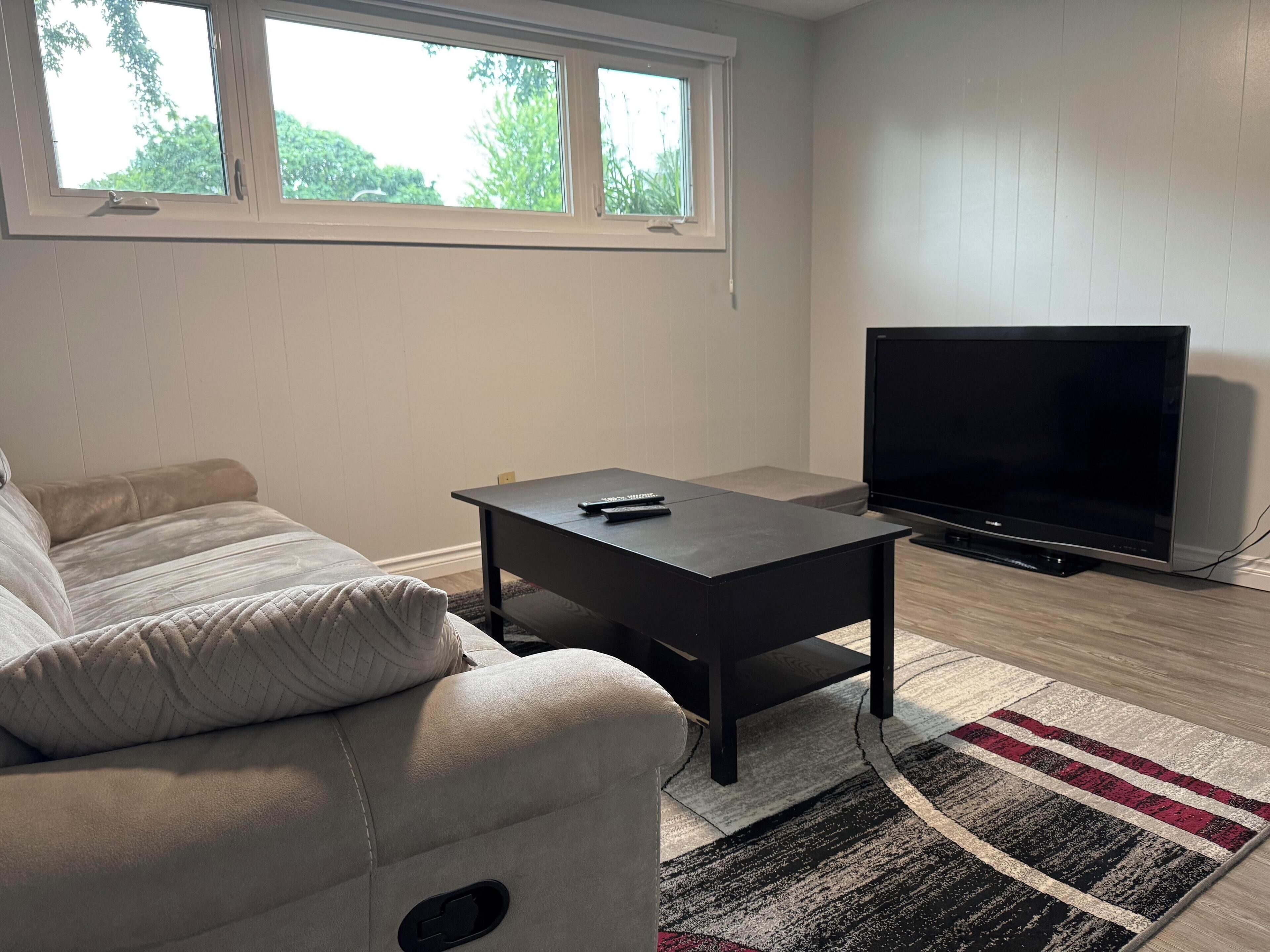 A living room with a sofa, a coffee table, a TV, and a window with a view of trees.