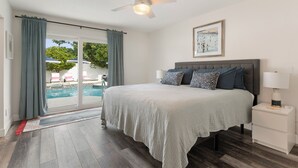 Un dormitorio con una cama grande, un ventilador de techo, una mesita de noche y vista a una piscina a través de un ventanal corredero.