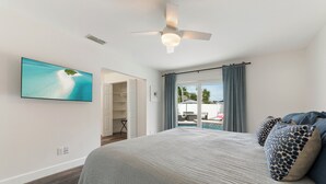 Un dormitorio con cama, ventilador de techo, televisor montado en la pared y vistas a una piscina y zona exterior.