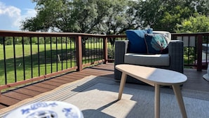 A deck with outdoor furniture, including a sofa and a small table, overlooking a green landscape. - Lux Home MINS to NE Baptist Hospital & TPC San Antonio/ Sleeps 4 (San Antonio)