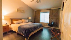 A bedroom with a bed, a ceiling fan, a window with curtains, a chair, and a wooden floor. - Lux Home MINS to NE Baptist Hospital & TPC San Antonio/ Sleeps 4 (San Antonio)