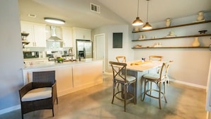 A modern kitchen with white cabinets, a central island, and a dining area with wicker chairs. - Lux Home MINS to NE Baptist Hospital & TPC San Antonio/ Sleeps 4 (San Antonio)
