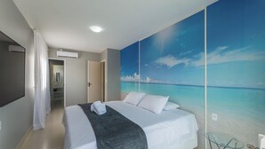 Hotellihuone, jossa on sänky, kylpyhuone ja suuri seinämaalaus, joka esittää rantamaisemaa.