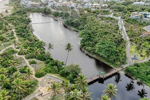 An aerial view of a river with a bridge, surrounded by greenery and residential buildings. - Casa c\/ Piscina e 6 Quartos em Camaraçi PJE0001 (Camaçari)