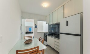 A compact kitchen with a refrigerator, stove, and a dining table with chairs. - Casa c\/ Piscina e 6 Quartos em Camaraçi PJE0001 (Camaçari)