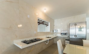 A modern kitchen with a gas stove, stainless steel appliances, and a large refrigerator. - Casa c\/ Piscina e 6 Quartos em Camaraçi PJE0001 (Camaçari)