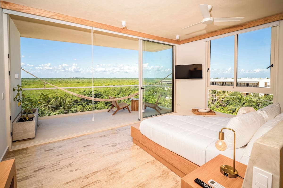 A modern bedroom with a large bed, a TV, and a balcony with a hammock.