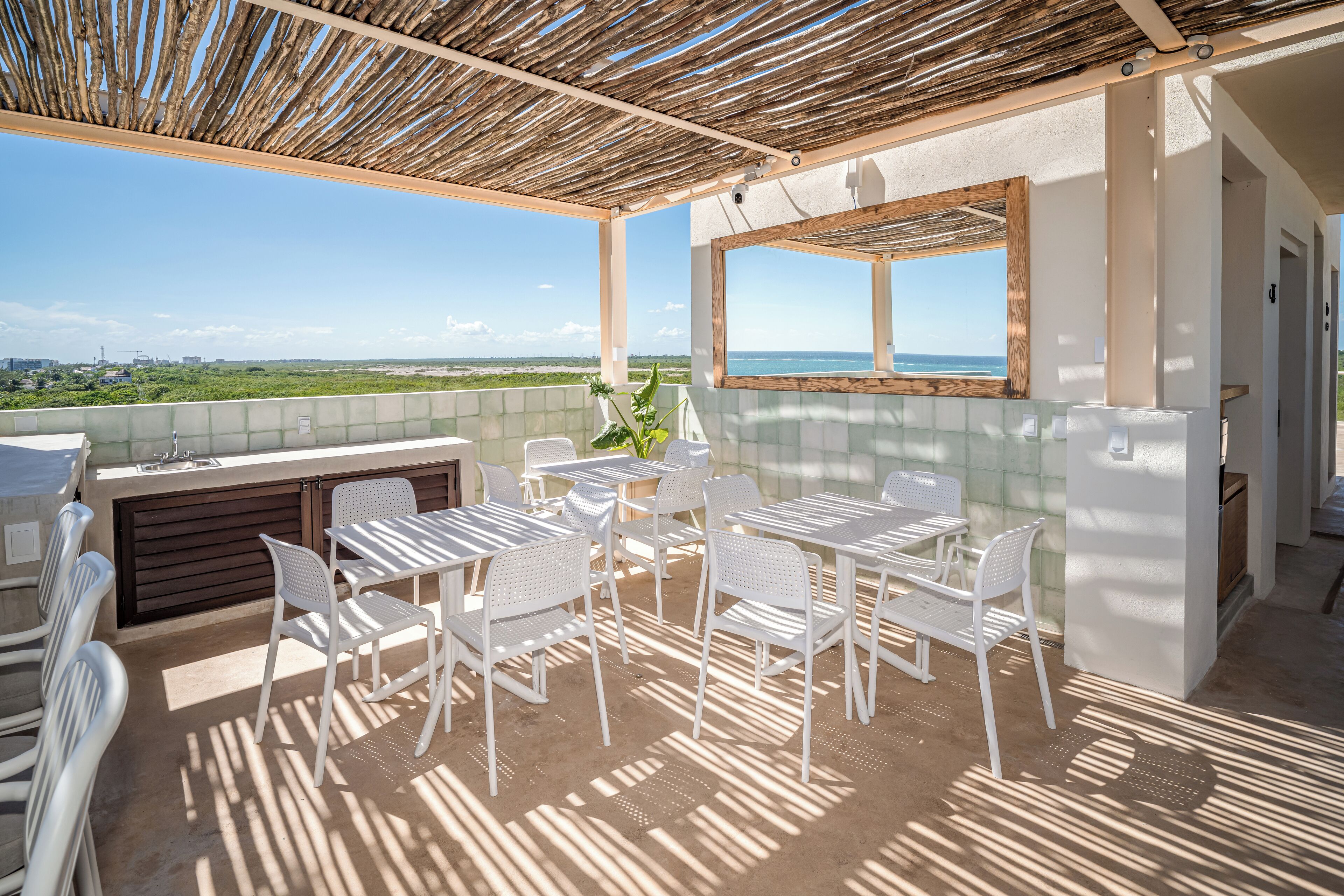 Eine Terrasse im Freien mit weißen Metallmöbeln, einer Holzpergola und Blick auf das Meer.