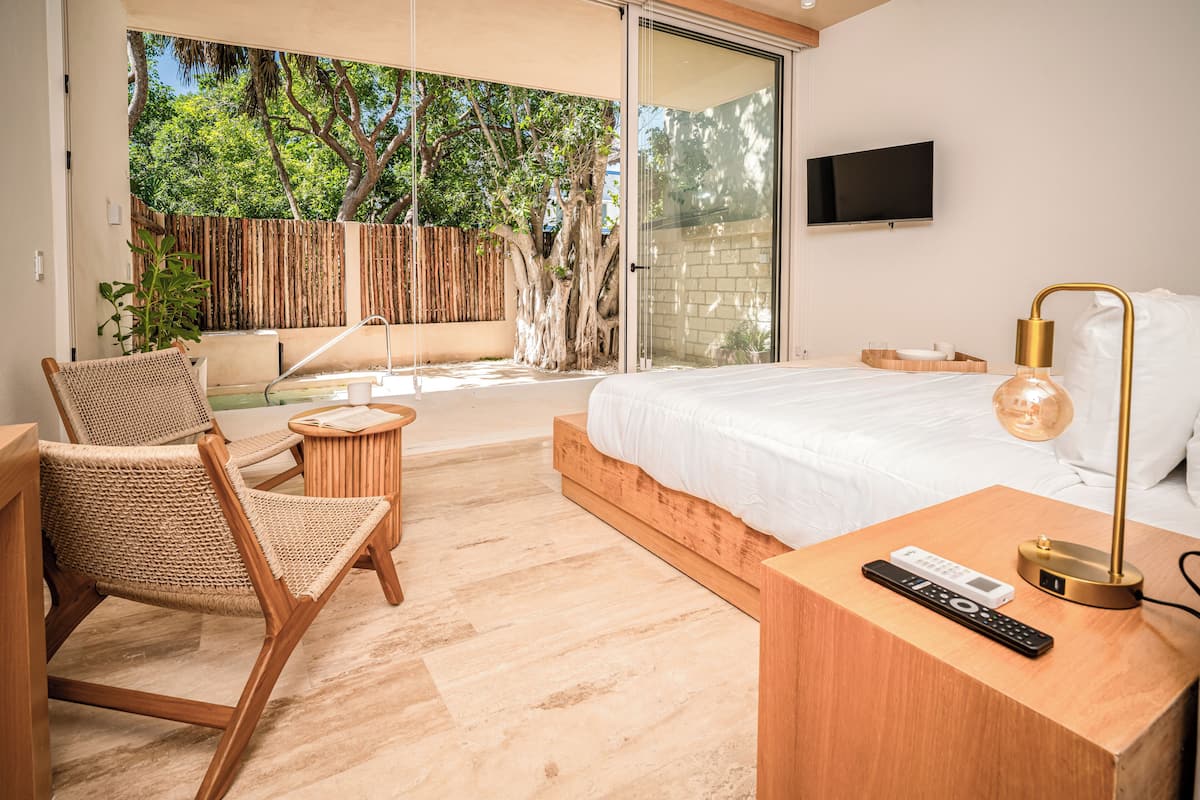 A modern bedroom with a large bed, a TV mounted on the wall, a wooden nightstand, and a wicker chair.
