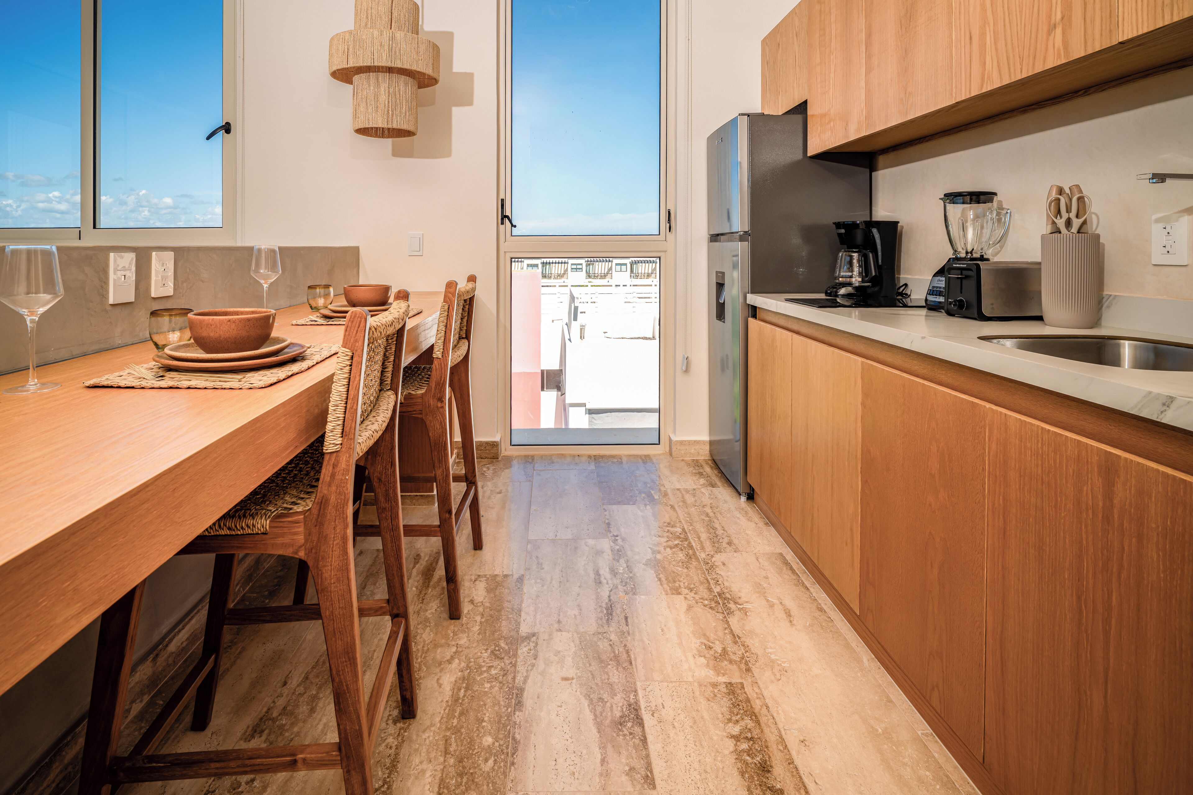 A modern kitchen with wooden cabinets, a stainless steel refrigerator, and a dining area with a wooden table and chairs.