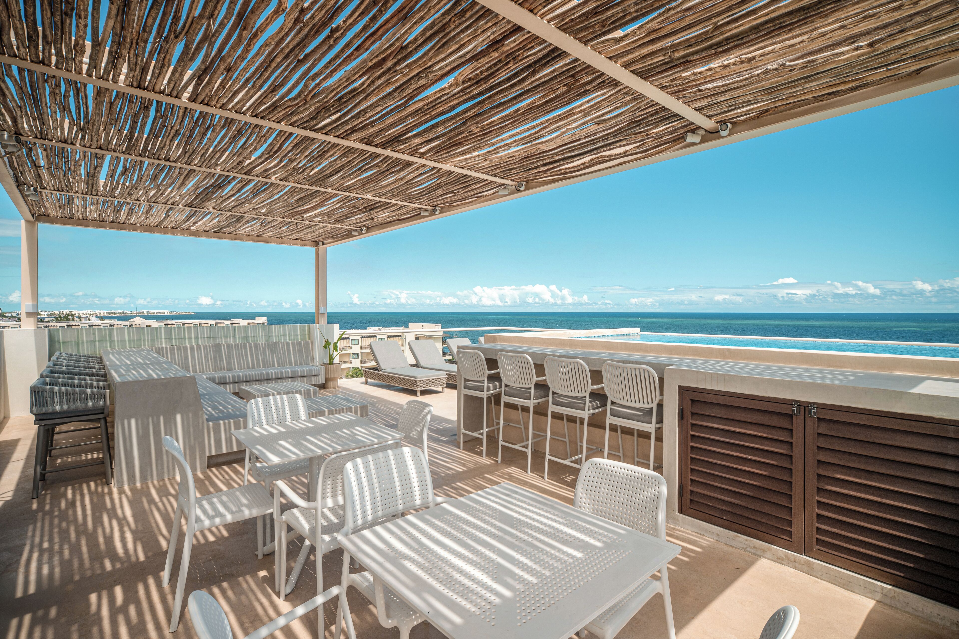 A rooftop terrace with outdoor seating, a view of the ocean, and a clear sky.