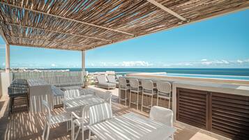 A rooftop terrace with outdoor seating, a view of the ocean, and a clear sky.