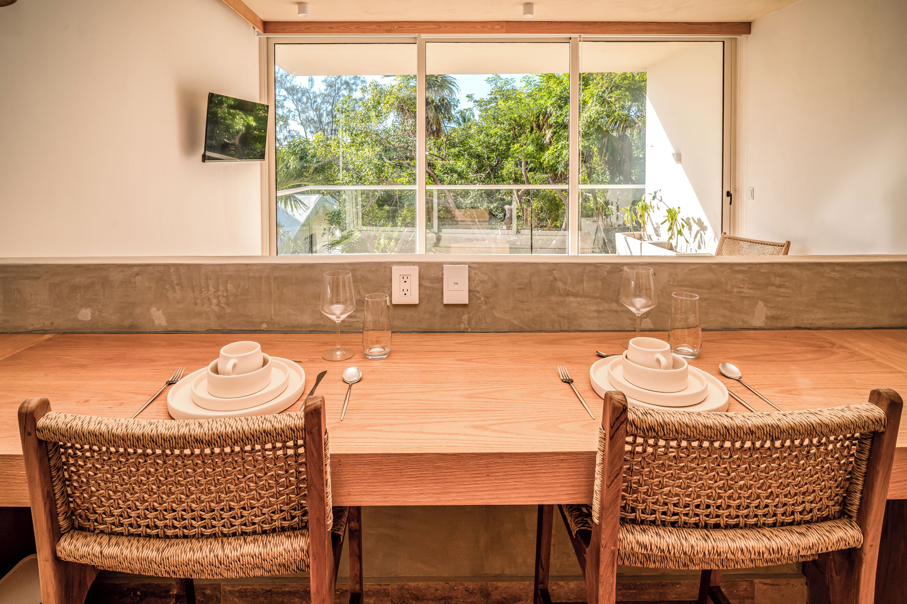 A dining table with two wicker chairs, a glass window, and a view of greenery outside.