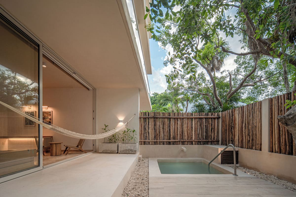A modern outdoor space with a glass door leading to a room, a hammock, a small pool, and a wooden fence.
