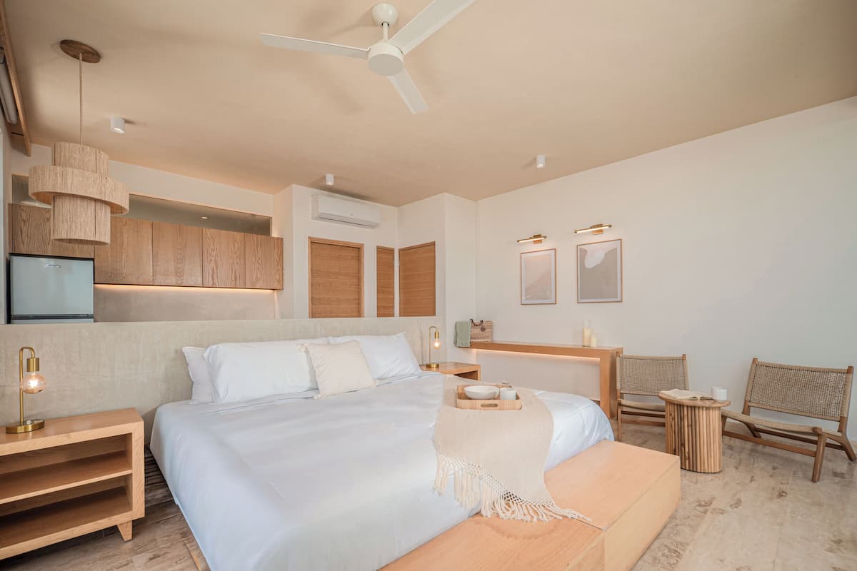 A modern hotel room with a large bed, a ceiling fan, a TV, and a small seating area with chairs and a table.