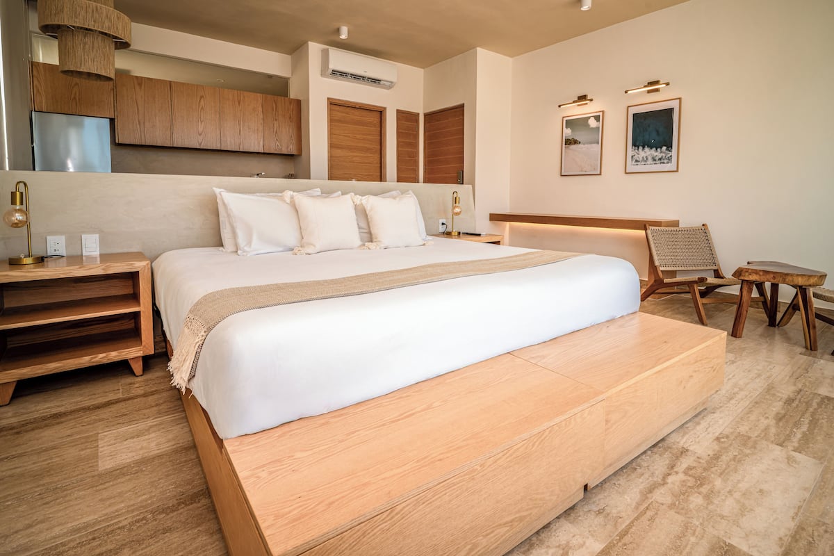 A modern bedroom with a large bed, wooden headboard, a small table, and a chair.