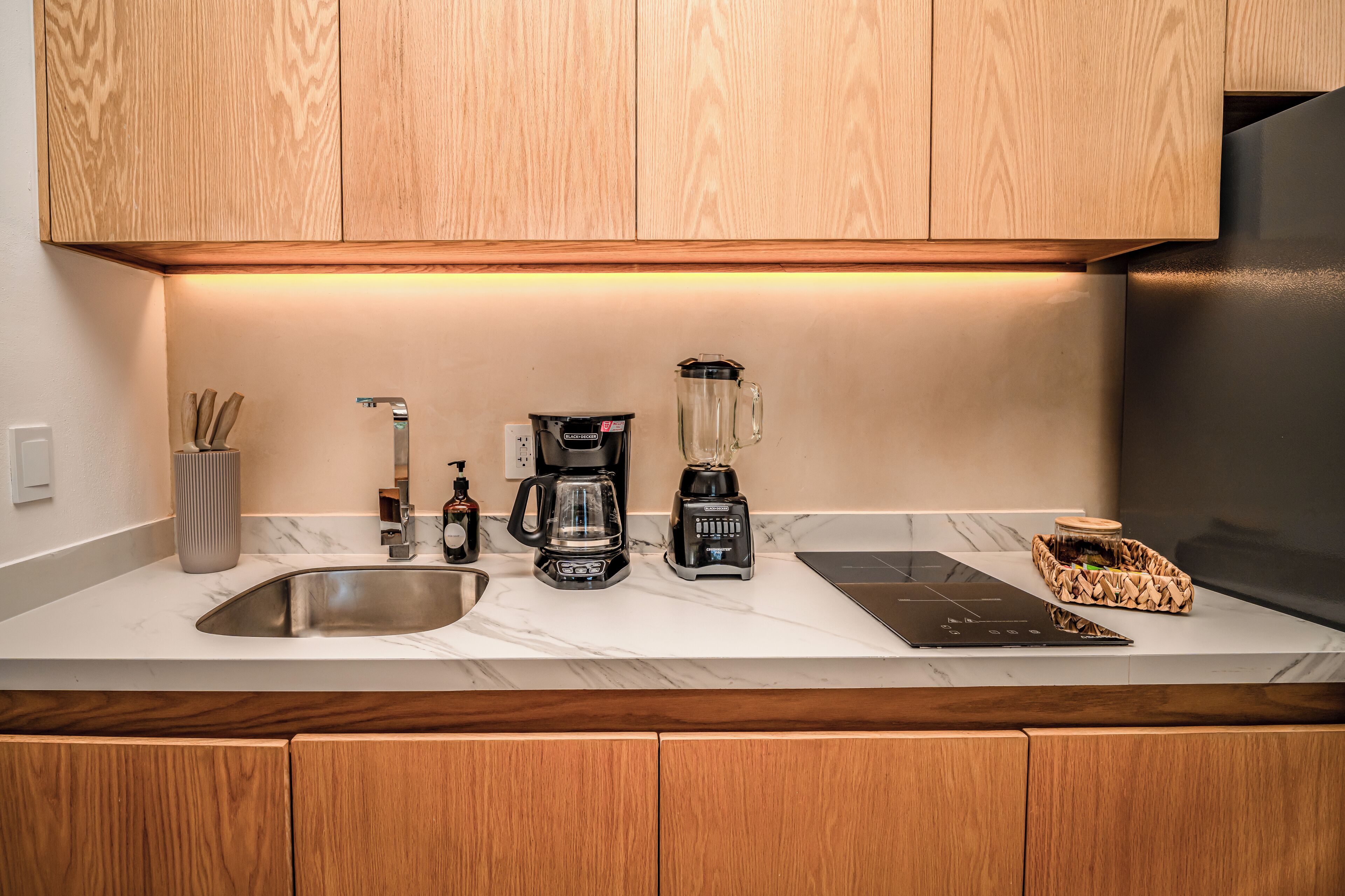 A modern kitchen with wooden cabinets, a stainless steel sink, a coffee maker, a blender, and a built-in induction cooktop.