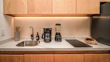 A modern kitchen with wooden cabinets, a stainless steel sink, a coffee maker, a blender, and a built-in induction cooktop.