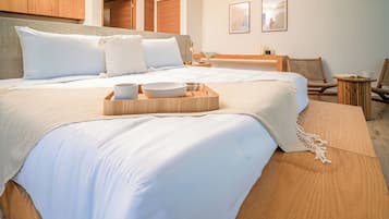 Una habitación de hotel con dos camas, cabecera de madera, mesita de noche con lámpara, una pequeña mesa redonda con bandeja y dos sillas de mimbre.