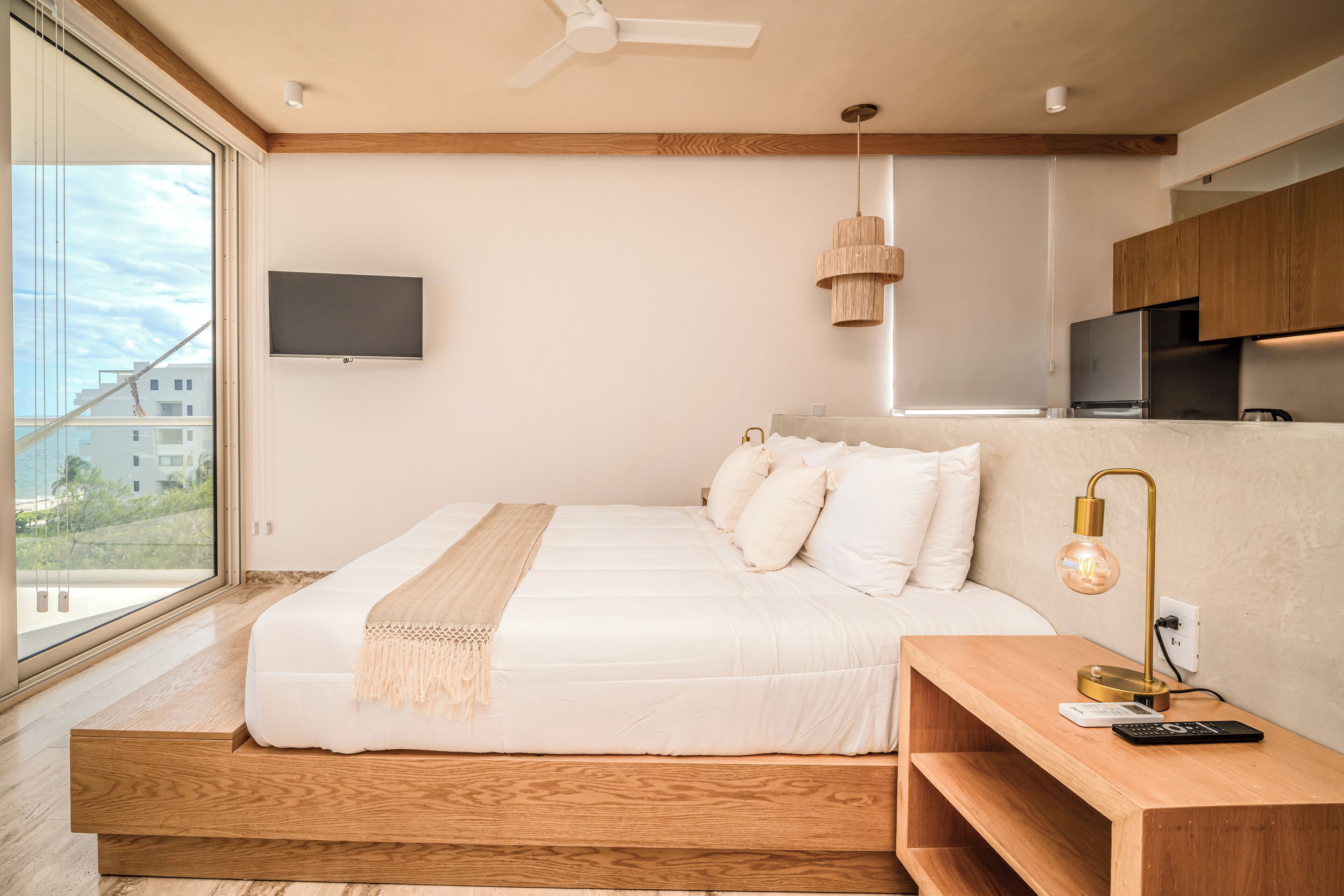 Un dormitorio moderno con una cama grande, un televisor montado en la pared y una mesita de noche de madera con una lámpara.
