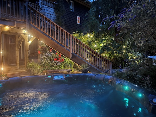 A hot tub with a wooden deck and stairs leading to a house.